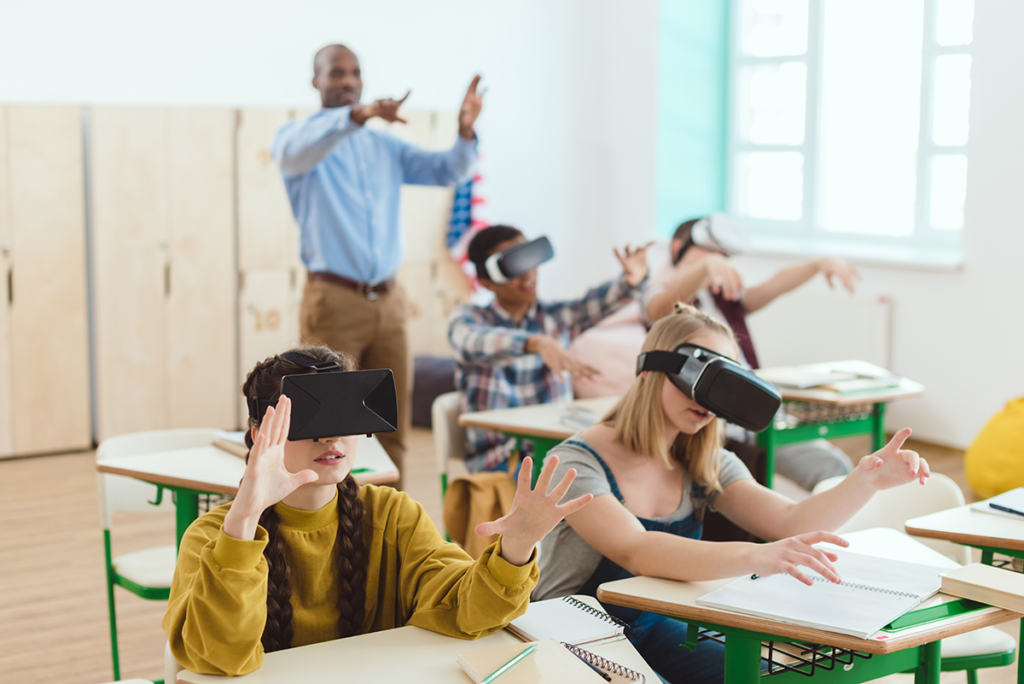 Kids at school desks using VR with teacher in background