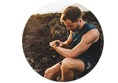 Man sitting on a rock wearing earbuds and checking his smart watch